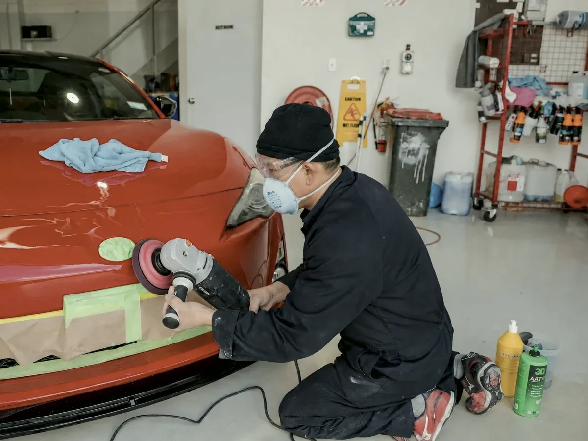 Technician in a respirator polishing a repaired front bumper at Fix Auto Mt Wellington