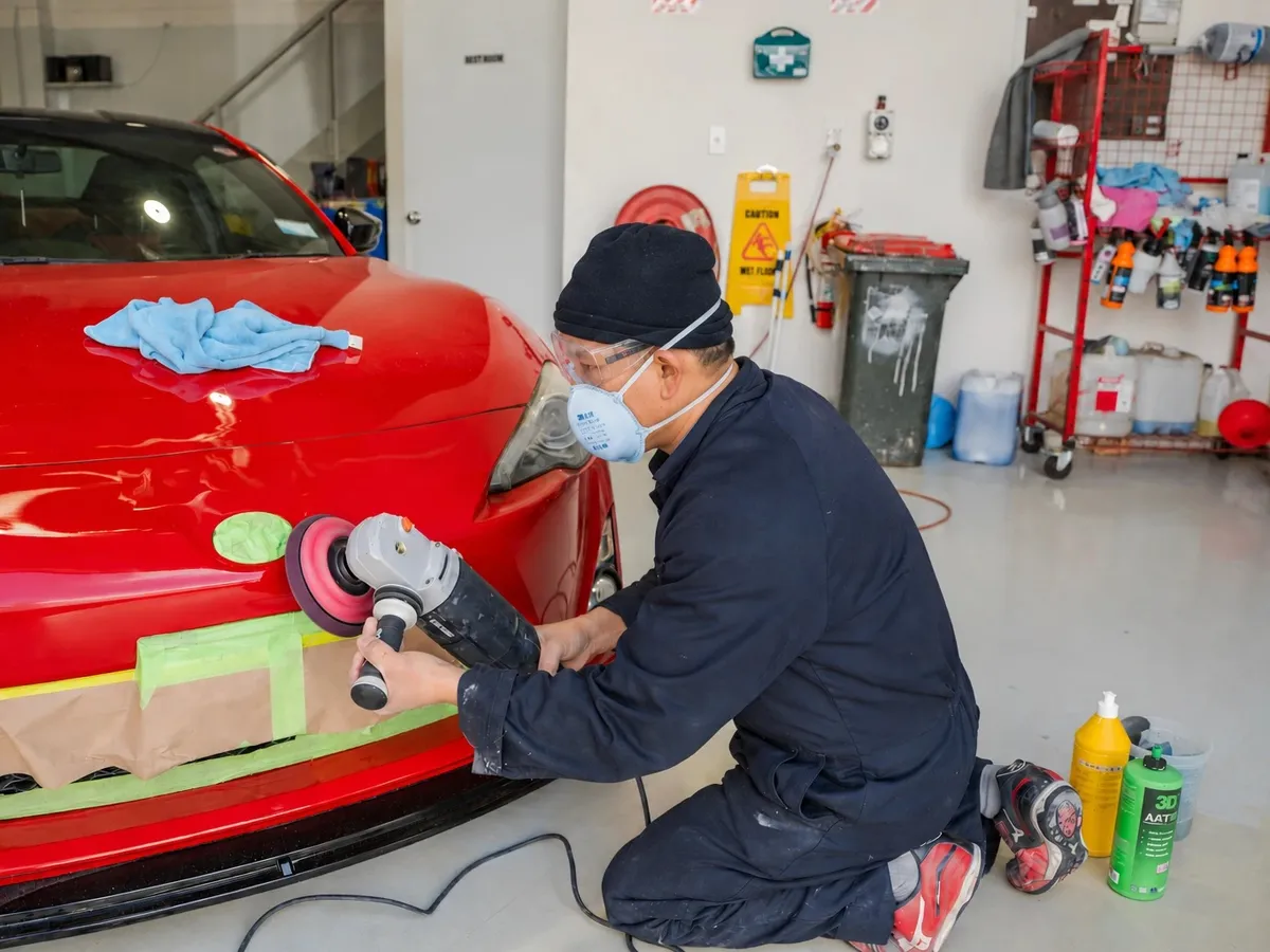 Technician in a respirator polishing a repaired front bumper at Fix Auto Mt Wellington